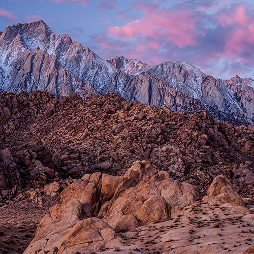 Rocky, red, snow-dusted mountains in the Sierra Nevada with a pink cloud sunrise